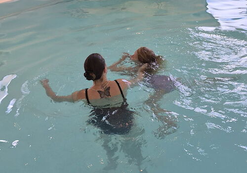 Frau lehrt Kind das Schwimmen in einem Hallenbad.