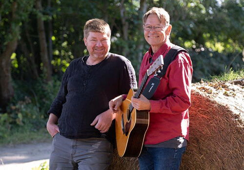 Zwei Männer, einer mit Gitarre, stehen neben Heuballen.