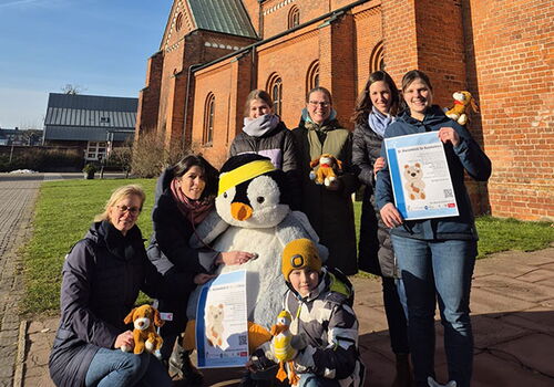 Gruppe posiert mit Pinguin vor roter Backsteinkirche.