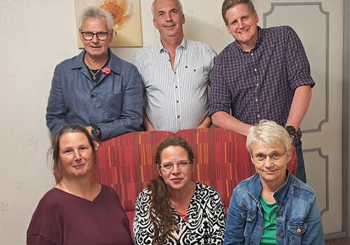 Sechs Personen posieren lächelnd für ein Gruppenfoto.