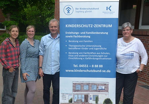 Vier Personen stehen neben einem Kinderschutz-Banner.