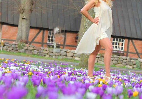 Frau im weißen Kleid posiert vor Fachwerkhaus und Krokusfeld.