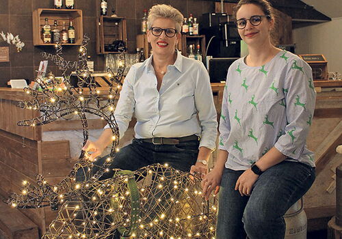Zwei Frauen sitzen auf einem leuchtenden Rentier im Café.