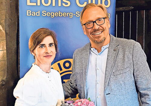Zwei Personen vor einem Lions Club-Banner mit Blumenstrauß.