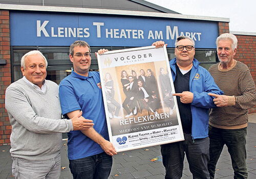 Vier Männer halten ein Konzertplakat vor einem kleinen Theater.