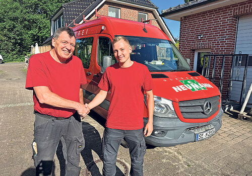 Zwei Männer schütteln Hände vor einem roten Lieferwagen.