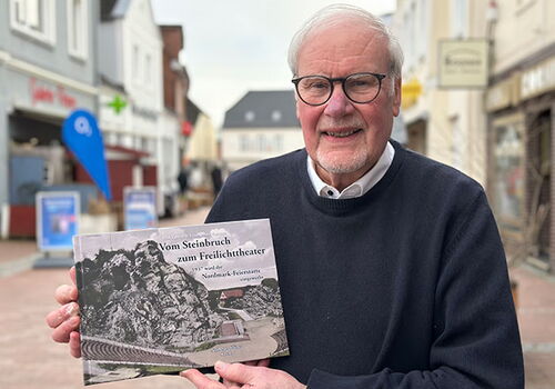 Mann hält ein Buch in einer belebten Einkaufsstraße.