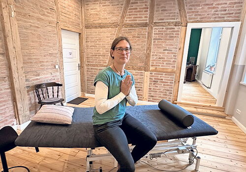 Frau sitzt mit gefalteten Händen auf einer Therapieliege.