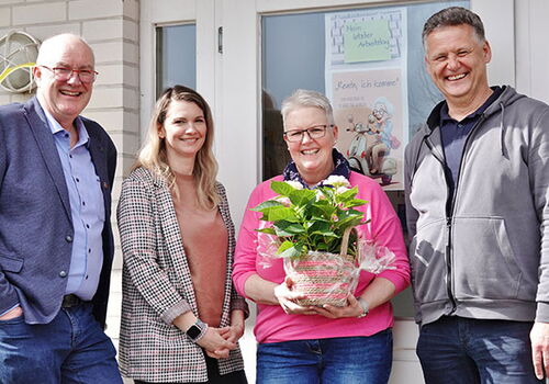 Vier Personen lächeln, eine hält eine Pflanze.