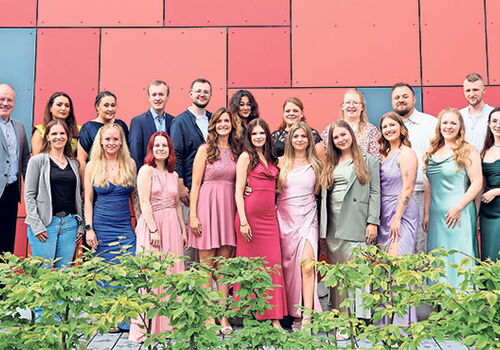 Gruppe von Menschen in eleganter Kleidung vor roter Wand.