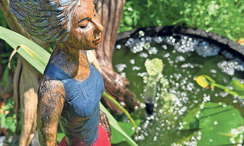 Bunte Holzfigur neben einem Teich mit Seerosen.