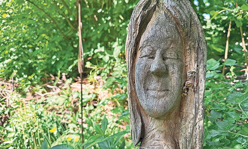 Holzskulptur eines Gesichts im grünen Garten