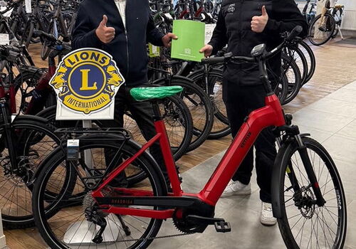 Zwei Männer stehen mit Daumen hoch neben einem roten Fahrrad.