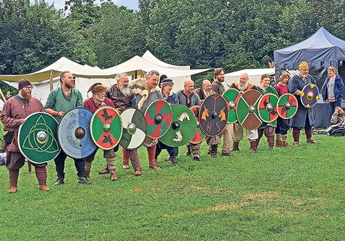 Menschen in Wikingerkostümen mit bunten Schilden im Freien.