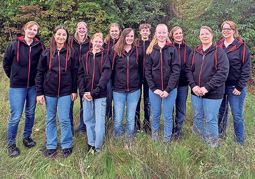 Eine Gruppe von zwölf Frauen in identischen schwarzen Hoodies.