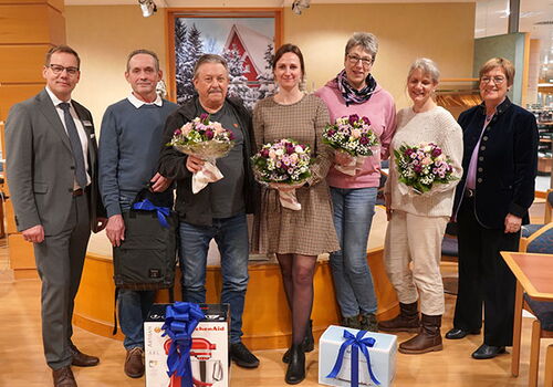 Sieben Personen posieren mit Geschenken und Blumensträußen.