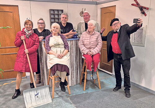 Gruppe von sieben Personen posiert fröhlich in einem Raum.