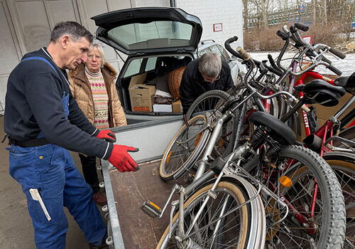 Drei Personen verladen Fahrräder auf einen Anhänger.