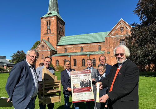 Gruppe vor Kirche mit Plakat für Benefizkonzert.