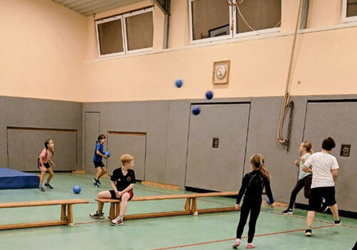 Kinder spielen mit Bällen in einer Turnhalle.
