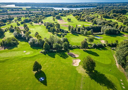 Luftaufnahme eines grünen Golfplatzes am See.