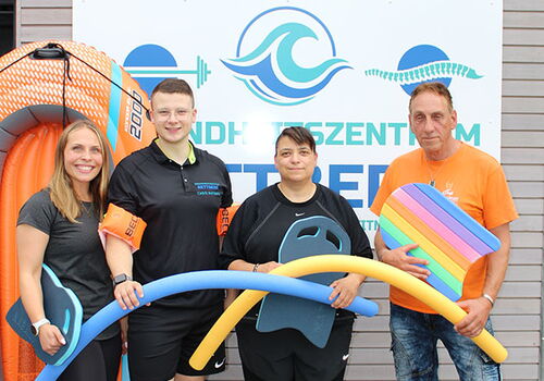 Vier Personen mit Schwimmausrüstung vor einem Schild