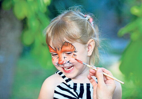 Lächelndes Kind mit Tiger-Gesichtsfarbe im Freien