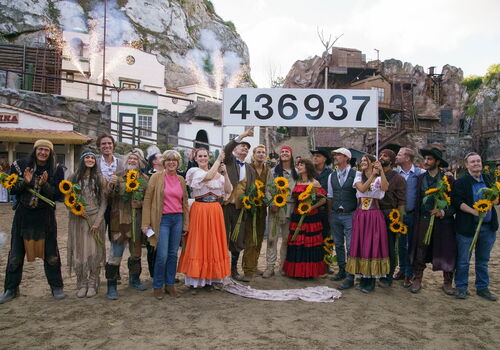 Gruppe posiert vor Kulisse mit Sonnenblumen und großer Zahl 436937.