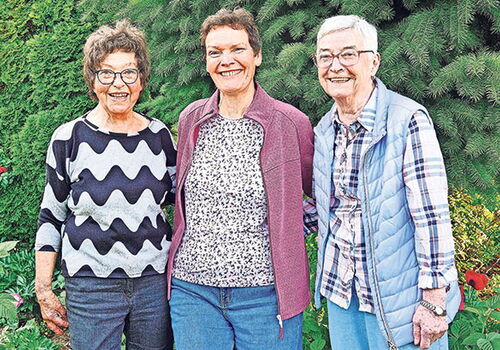 Drei lächelnde Frauen stehen in einem Garten.