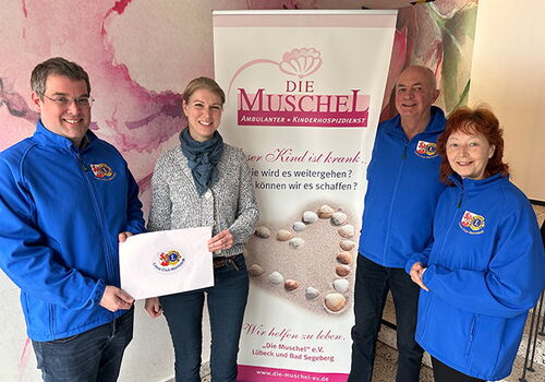 Vier Personen stehen vor einem Banner von 'Die Muschel'.