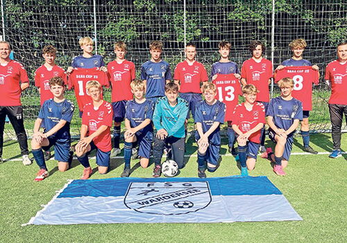 Fußballteam posiert mit Vereinsflagge auf dem Spielfeld.