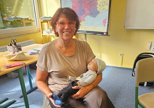 Frau hält Puppe in einem Klassenzimmer mit Frankreichkarte.