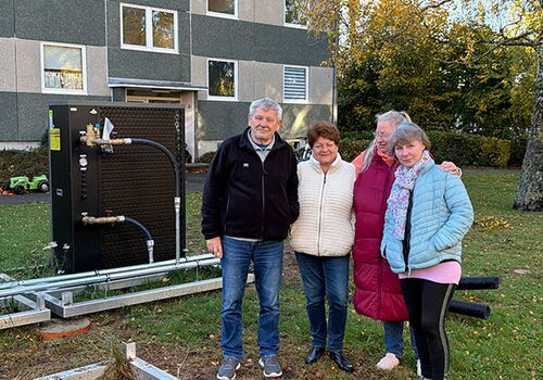 Vier Menschen vor einem Gebäude mit Wärmepumpe im Freien.