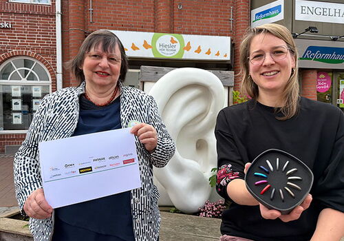 Zwei Frauen vor Skulptur eines überdimensionalen Ohrs in der Stadt.