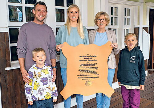 Fünf Personen halten eine Ehrentafel vor einem Gebäude.