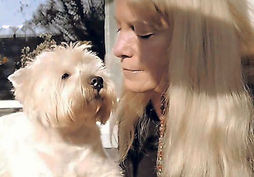 Frau mit langem Haar blickt liebevoll auf einen weißen Hund.