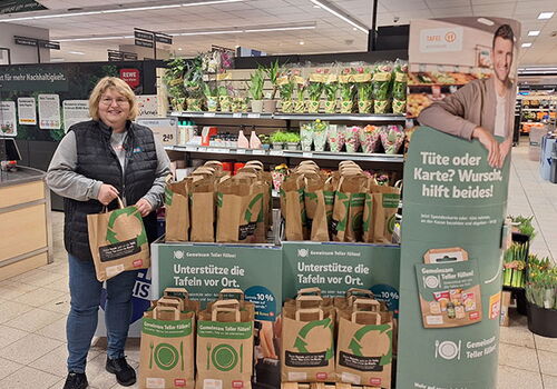Frau hält Einkaufstasche neben Tafeln-Spendenstand.
