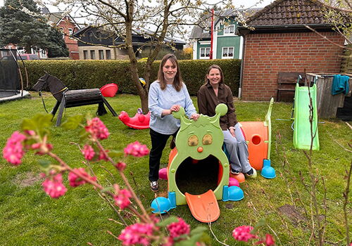 Zwei Frauen im Garten mit Kinderrutsche und Spielzeugpferd.