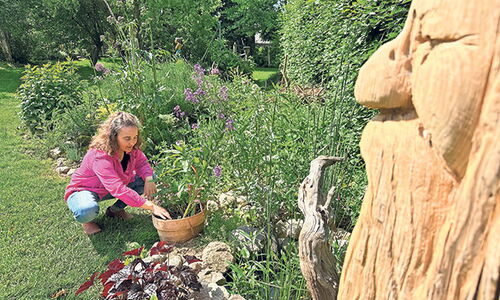 Steffi Weilkiens im Garten mit Blumen und Holzfigur