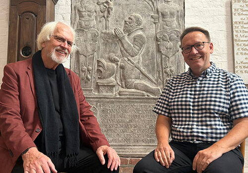 Zwei Männer sitzen vor einem historischen Relief in der Kirche.