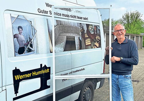 Mann steht neben einem Firmenwagen mit Text und Logo.