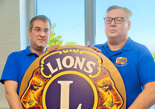 Zwei Männer halten ein Lions Club International Emblem.