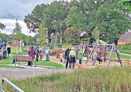 Kinder spielen auf einem Spielplatz, Erwachsene schauen zu.