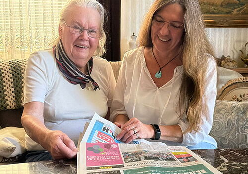 Zwei Frauen lesen gemeinsam eine Zeitung auf dem Sofa.