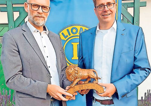 Zwei Männer halten eine Holzfigur eines Löwen.