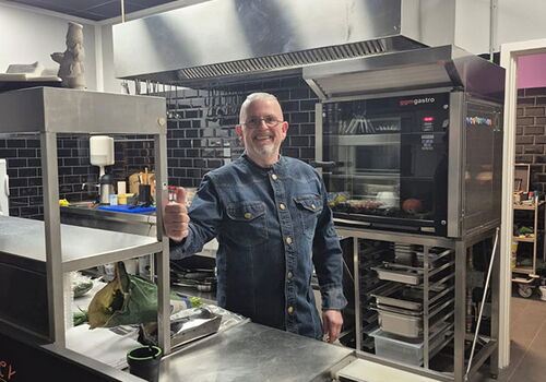 Mann in Küche zeigt Daumen hoch neben Edelstahlgeräten.