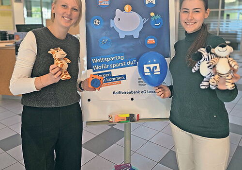 Zwei Frauen mit Spielzeug vor einem Weltspartag-Poster.
