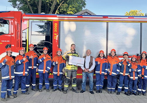 Gruppe vor Feuerwehrauto hält einen Scheck