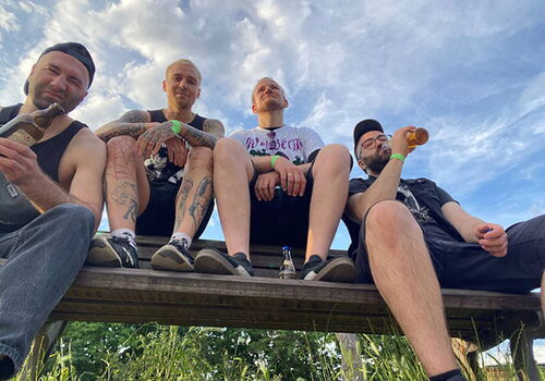 Vier Männer sitzen auf einem Holzgerüst und trinken Bier.