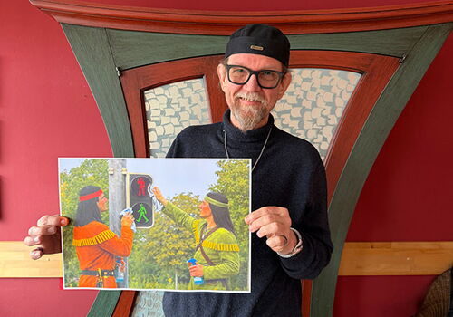 Mann hält Bild von zwei sich grüßenden Figuren an Ampel.